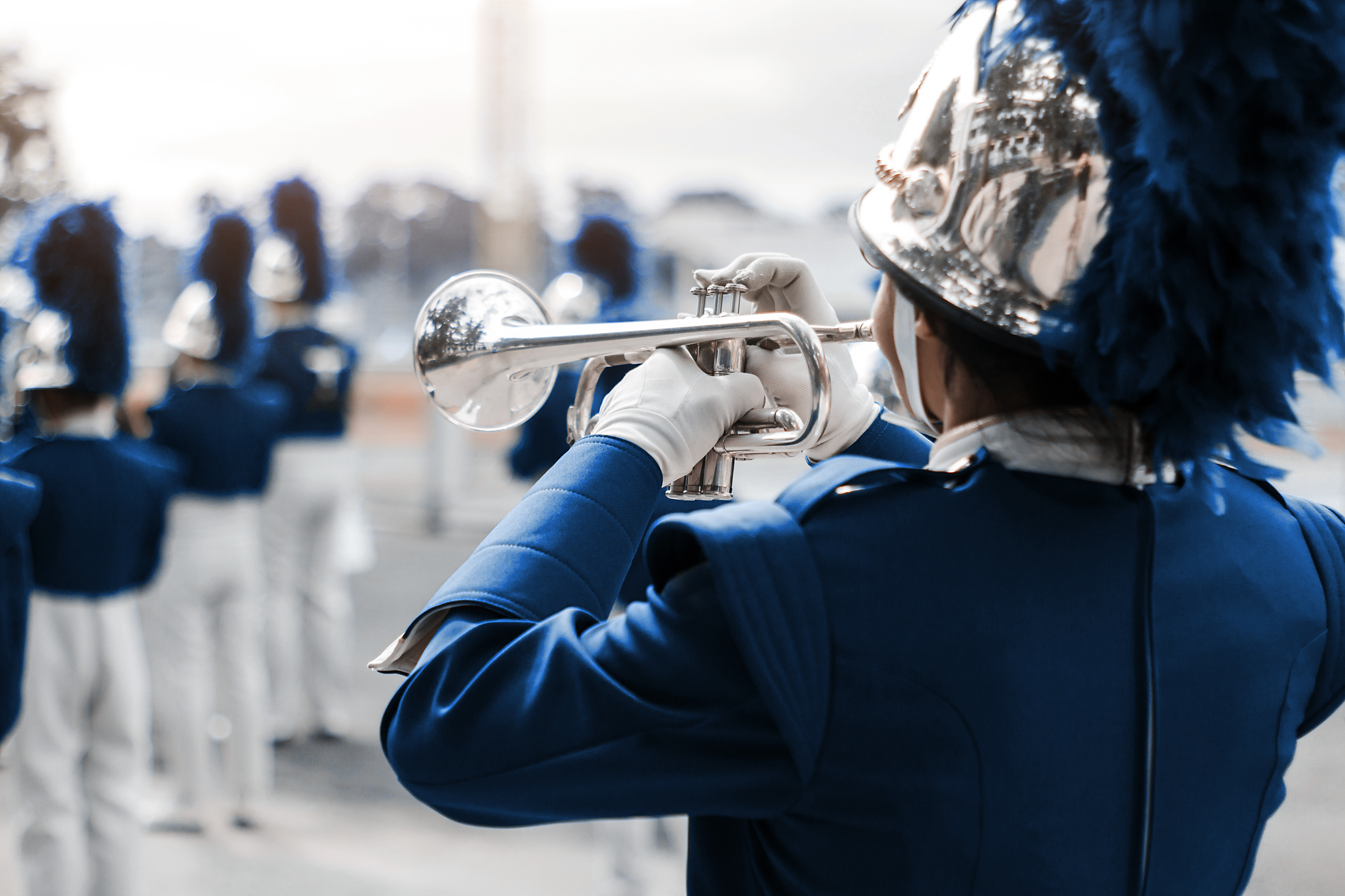 Marching band member in a blue uniform playing a trumpet, with other band members blurred in the background